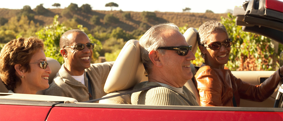 Four people smile as they travel in a convertable 