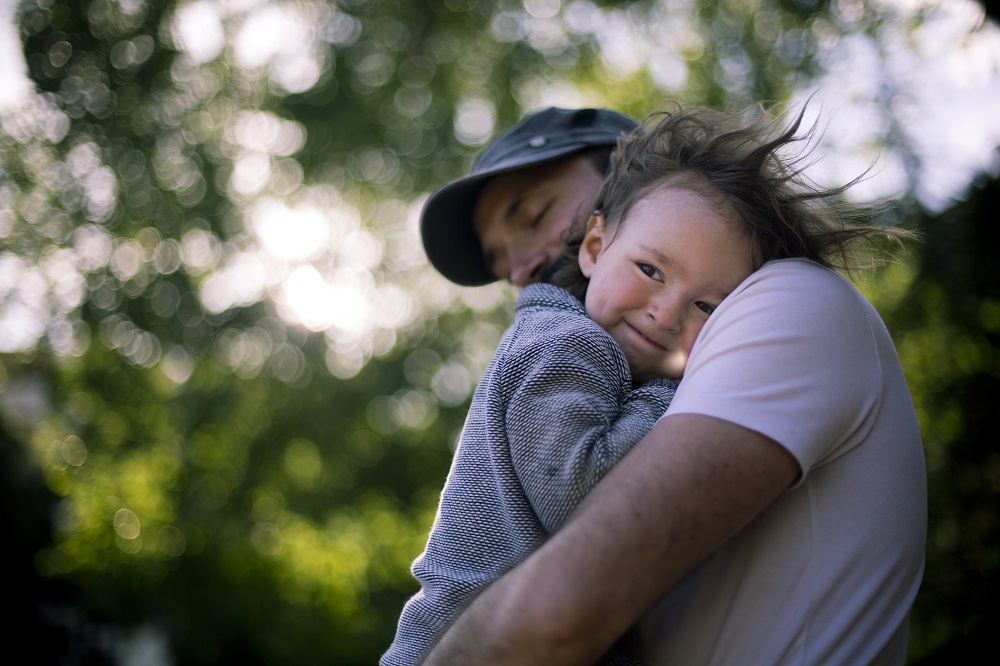 A father hugging his smiling son outdoors.