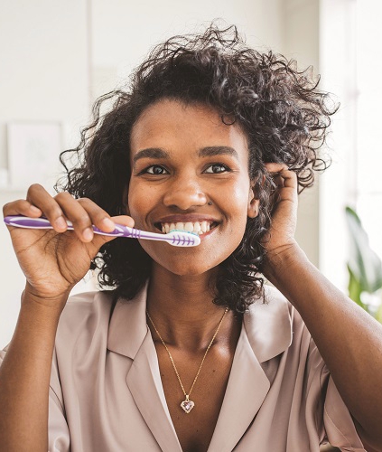 Woman smiling while brushing her teeth.