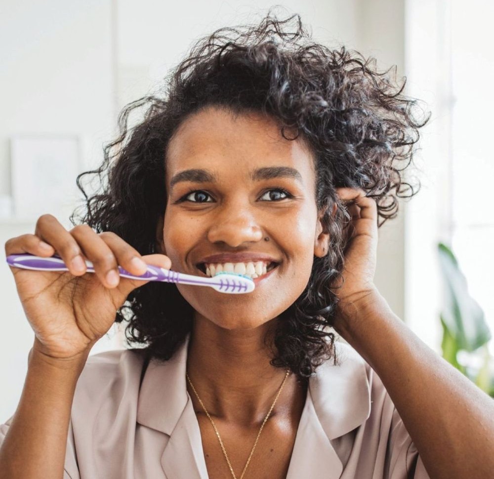 Woman smiling while brushing her teeth.