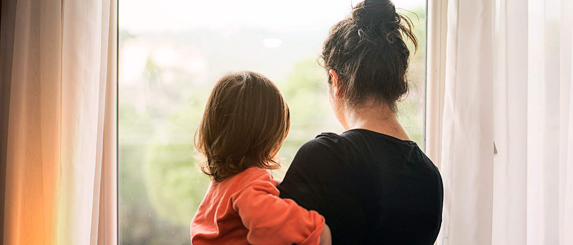 Woman faces a window as she holds a child