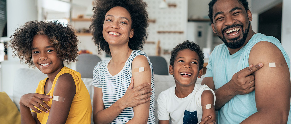 Parents and young son and daughter smile and show arms with Band-Aids from vaccine shots.