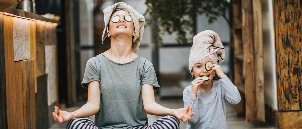 A young woman with cucumber slices covering her eyes and a child sitting in yoga positions