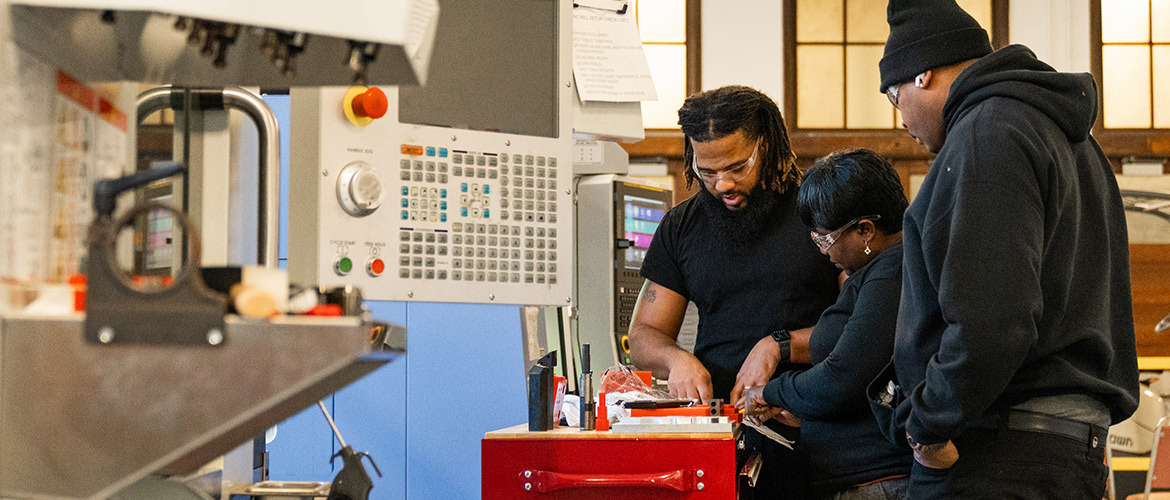 A man instructs students on a piece of machinery