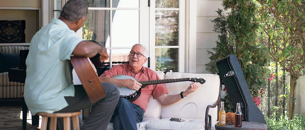 Two men play instruments while sitting on a porch