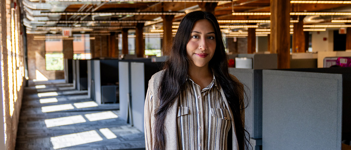 Young woman with dark hair stands in sunlit, modern loft office 
