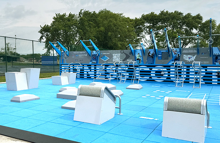 Outdoor exercise equipment is shown in a park with trees in the background 