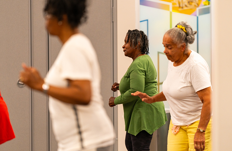 Three older women practice line-dancing steps. 