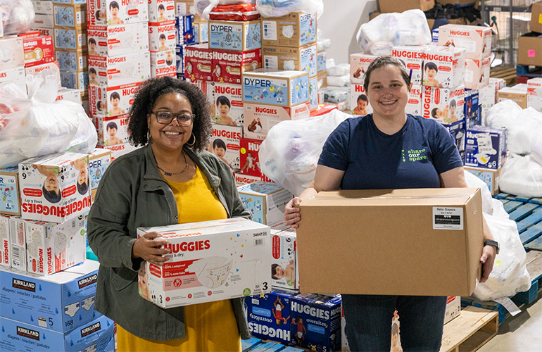 Share Our Spare employees pose with diapers at the warehouse