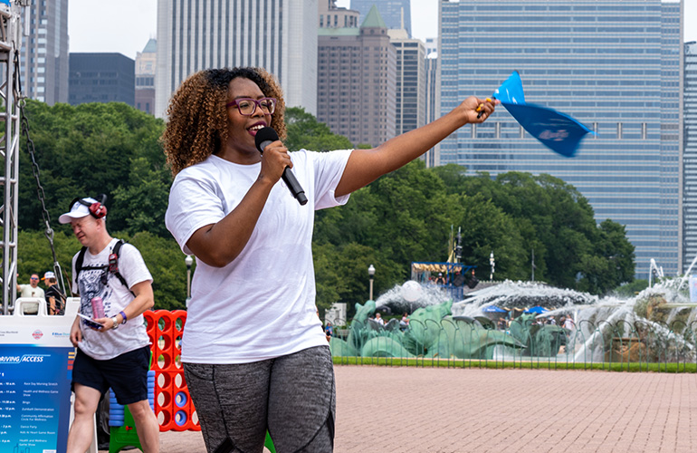 African American woman with microphone encourages NASCAR fans to join excercises.