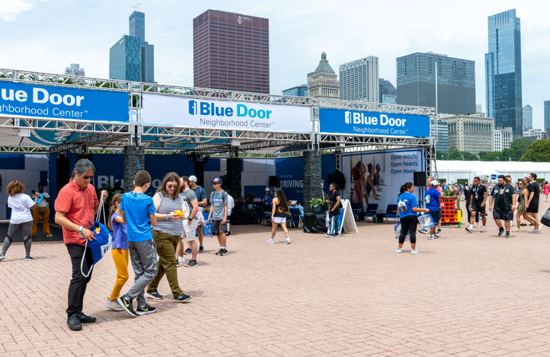 Event attendees walk by a pop-up Blue Door Neighborhood Center with Chicago’s skyline in the background.