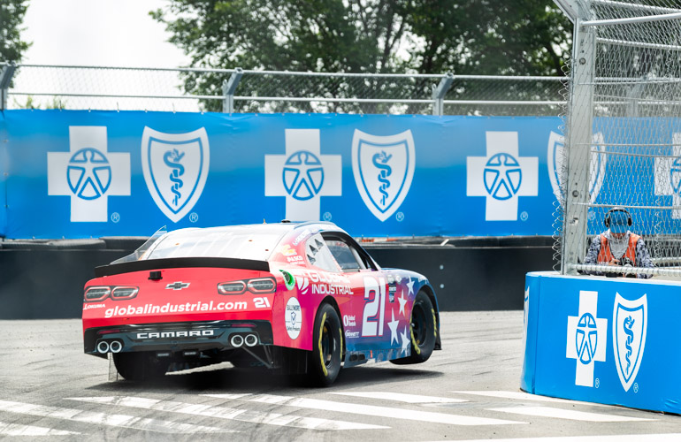 A red racecar’s tires lift off the ground as it rounds a bend.