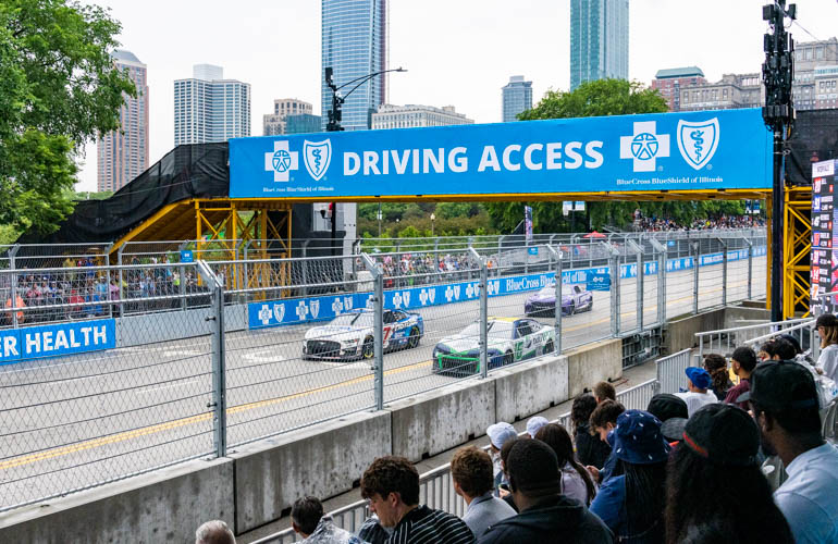 The words Driving Access are shown in white letters on a blue background with the BCBSIL logo on a pedestrian bridge over the racecourse. 