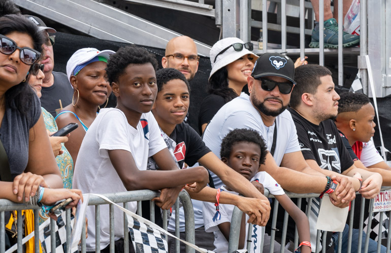 A crowd gathers against a barrier at the street level to view the race.