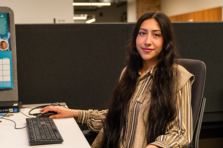 Young woman at work sitting at desk looks into camera