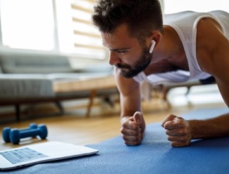 Young man doing a plank exercise on his living room rug, watching an exercise video or live feed on his laptop.
