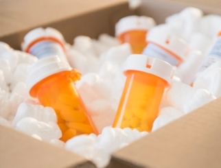 Caja de cartón con seis frascos de color naranja con medicamentos, envueltos en bolitas de poliestireno