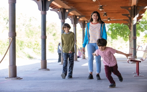 Imagen de una mujer con dos hijos caminando bajo la pérgola de un parque