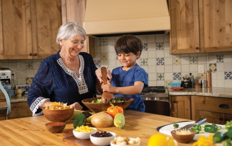 Image of a young boy helping a grandmother stir food in a bowl