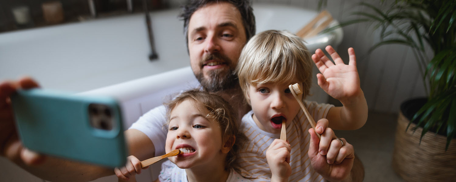 Father brushing teeth with children while taking a photo