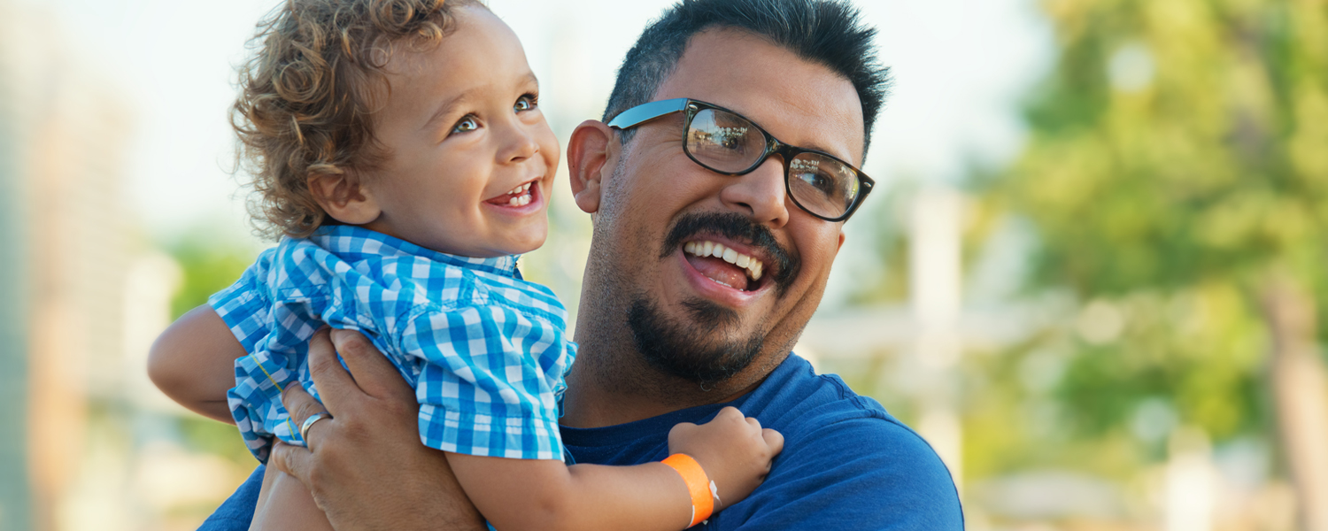 A man in glasses smiles while holding a small boy
