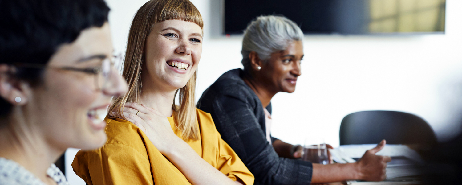 A woman smiles at a conference table with other people