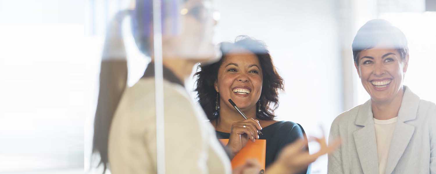 Two women smile widely while another speaks in the foreground