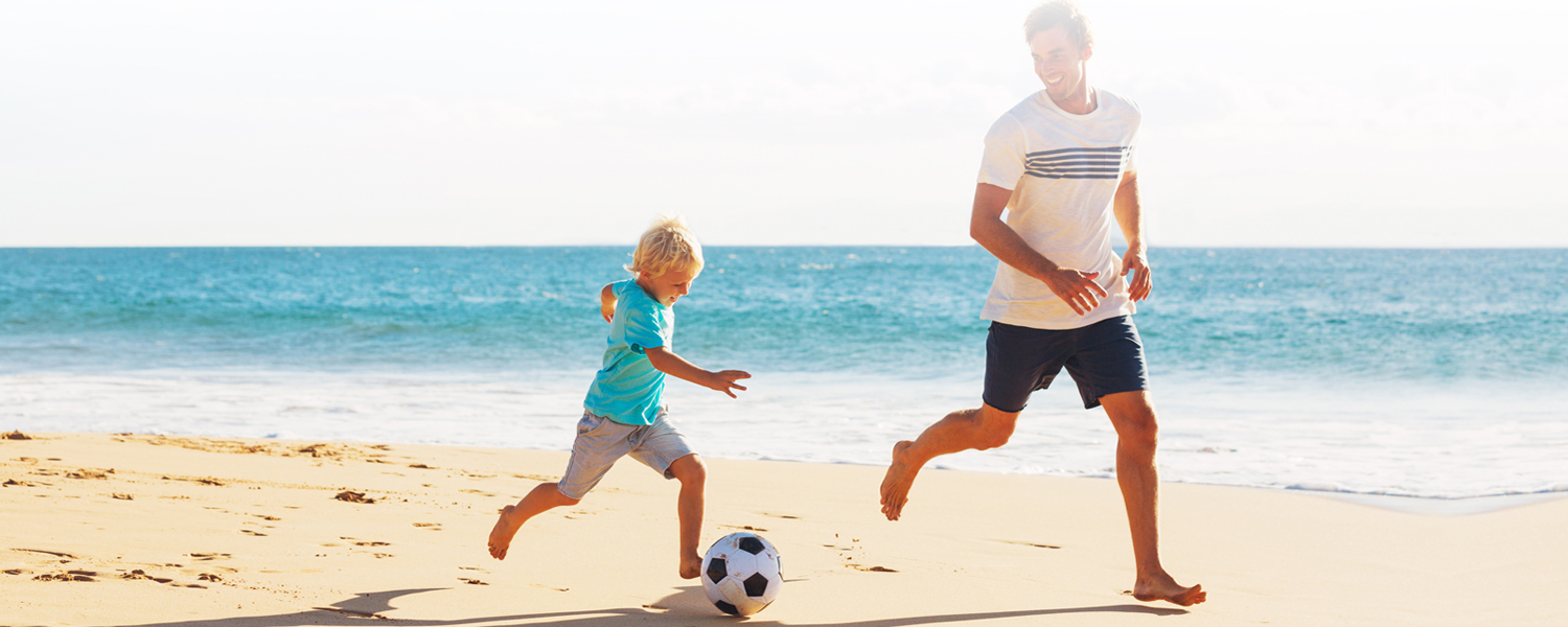 A man and small boy play with a soccer ball on the beach