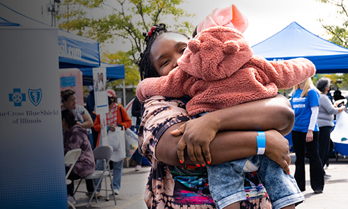 An African American woman hugs a toddler at a block party at a Blue Door Neighborhood Center. 