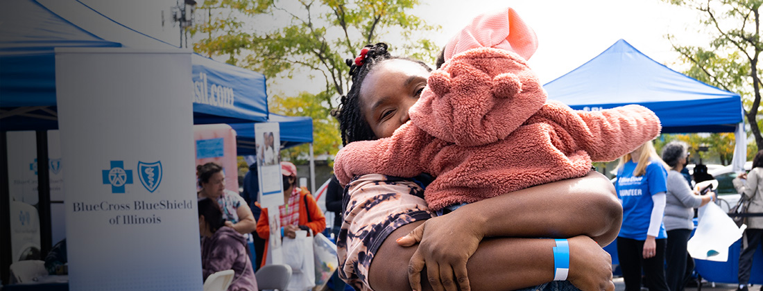 An African American woman hugs a toddler at a block party at a Blue Door Neighborhood Center. 