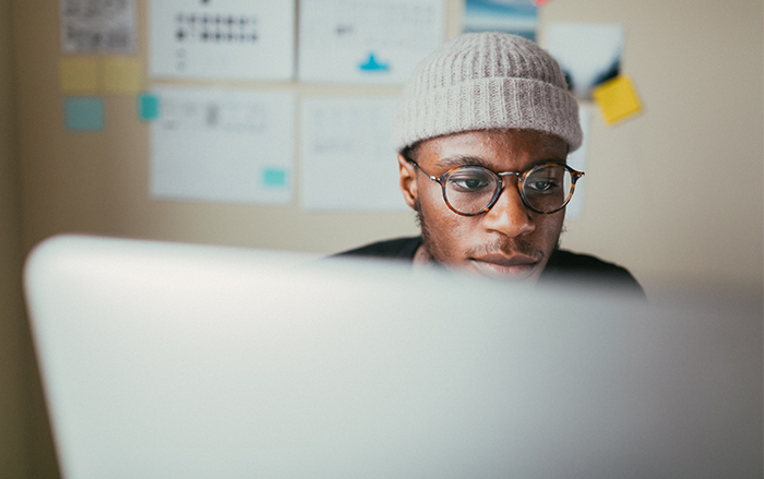 Hombre afroamericano con gorro en una oficina mira atentamente una computadora.