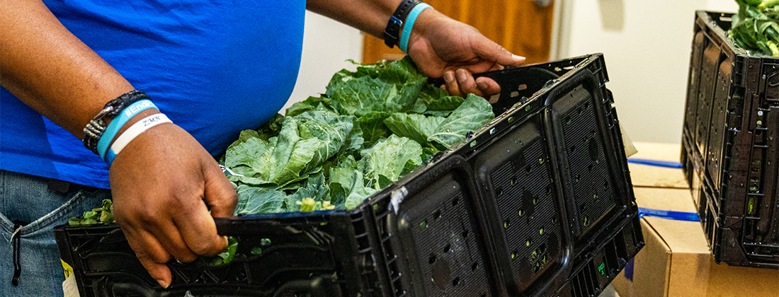 Un hombre lleva una caja de vegetales de hojas verdes