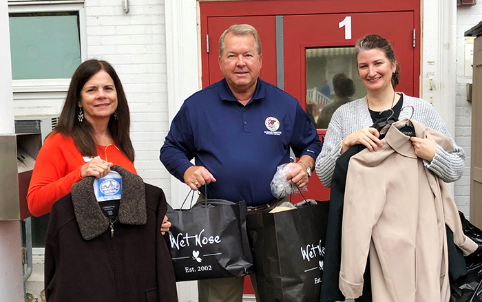 Three people pose with donated coats and goods