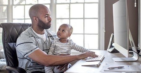 Imagen de un hombre que usa una computadora y sostiene un bebé