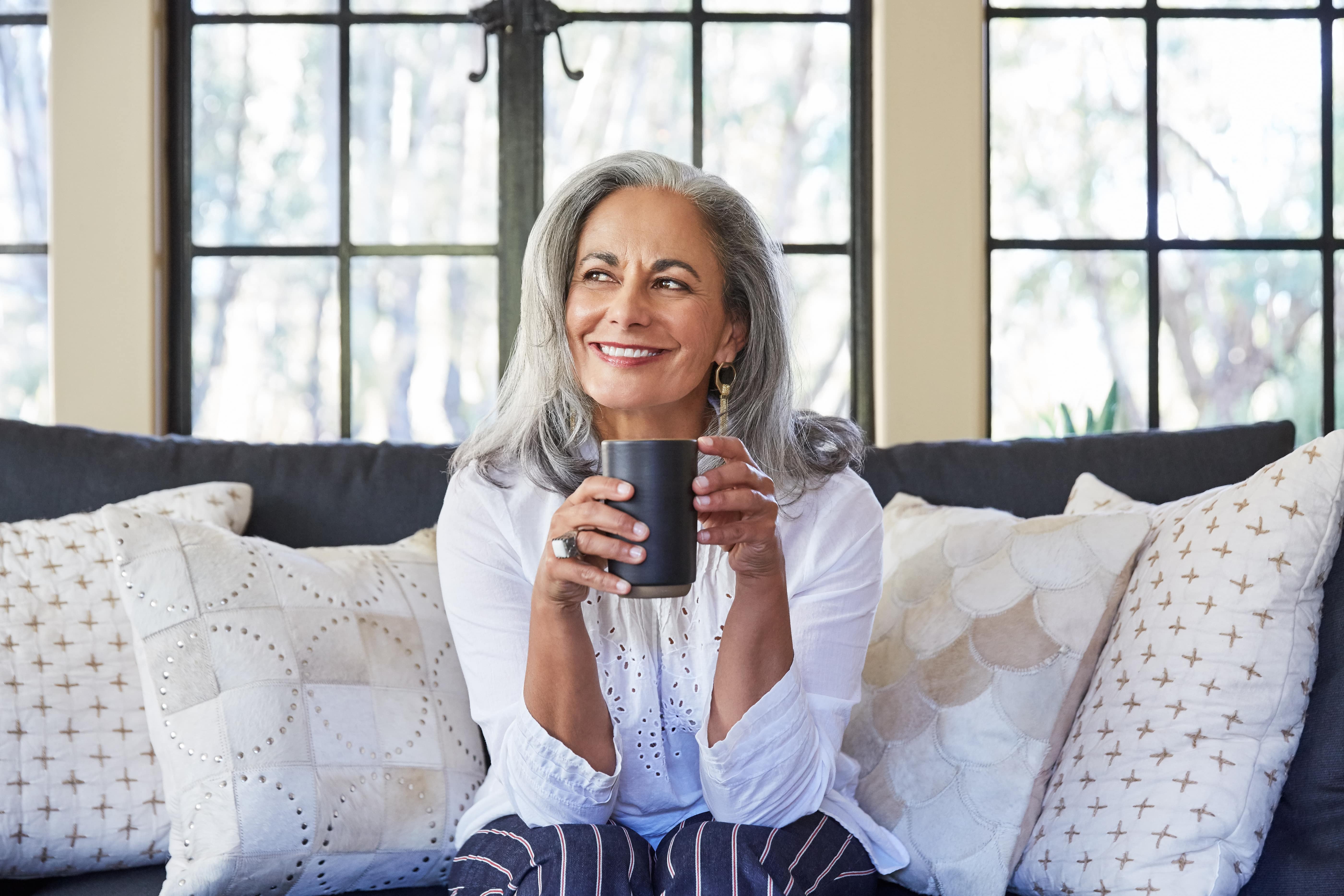 Mujer mayor sentada en el sofá, sonriendo y con una taza de café en la mano