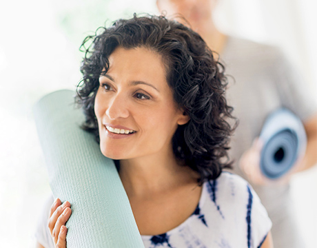Image of a woman holding a yoga mat on her shoulder