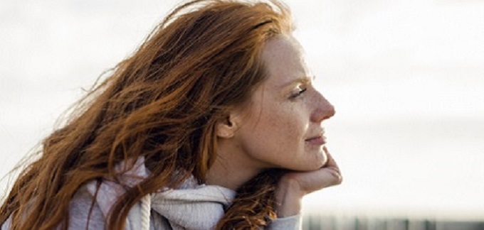 Woman with red hair resting with her head on her hand.