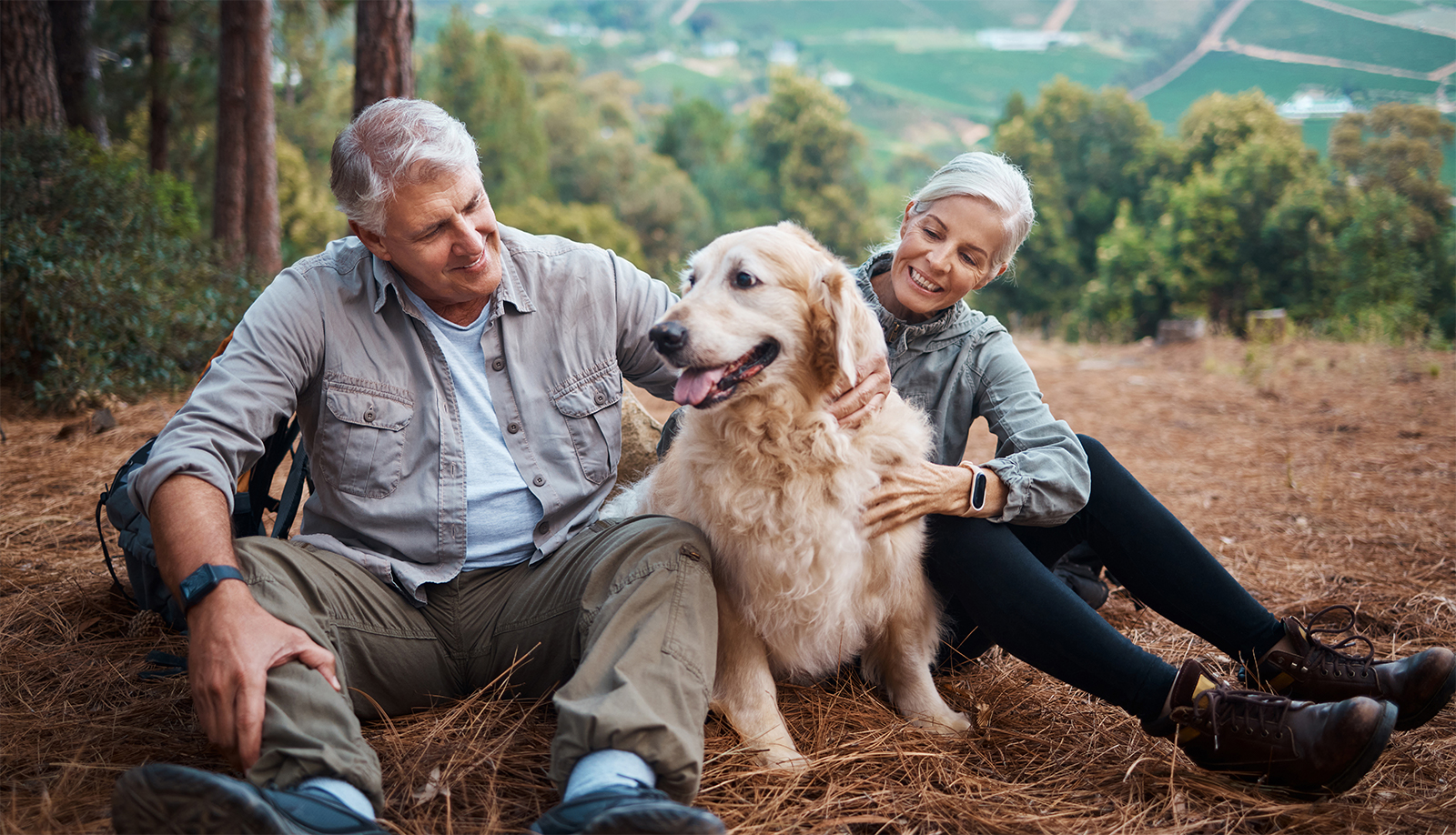 Senior couple petting a dog while taking a break during a hike on a mountain.